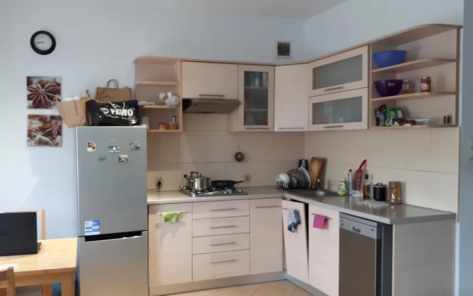 Kuchnia w wynajmowanym mieszkaniu w Łodzi: jasne szafki, lodówka, kuchenka i zlew