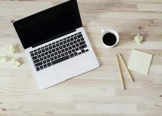 Laptop, kubek kawy, notes i ołówki na jasnym drewnianym stole, z góry